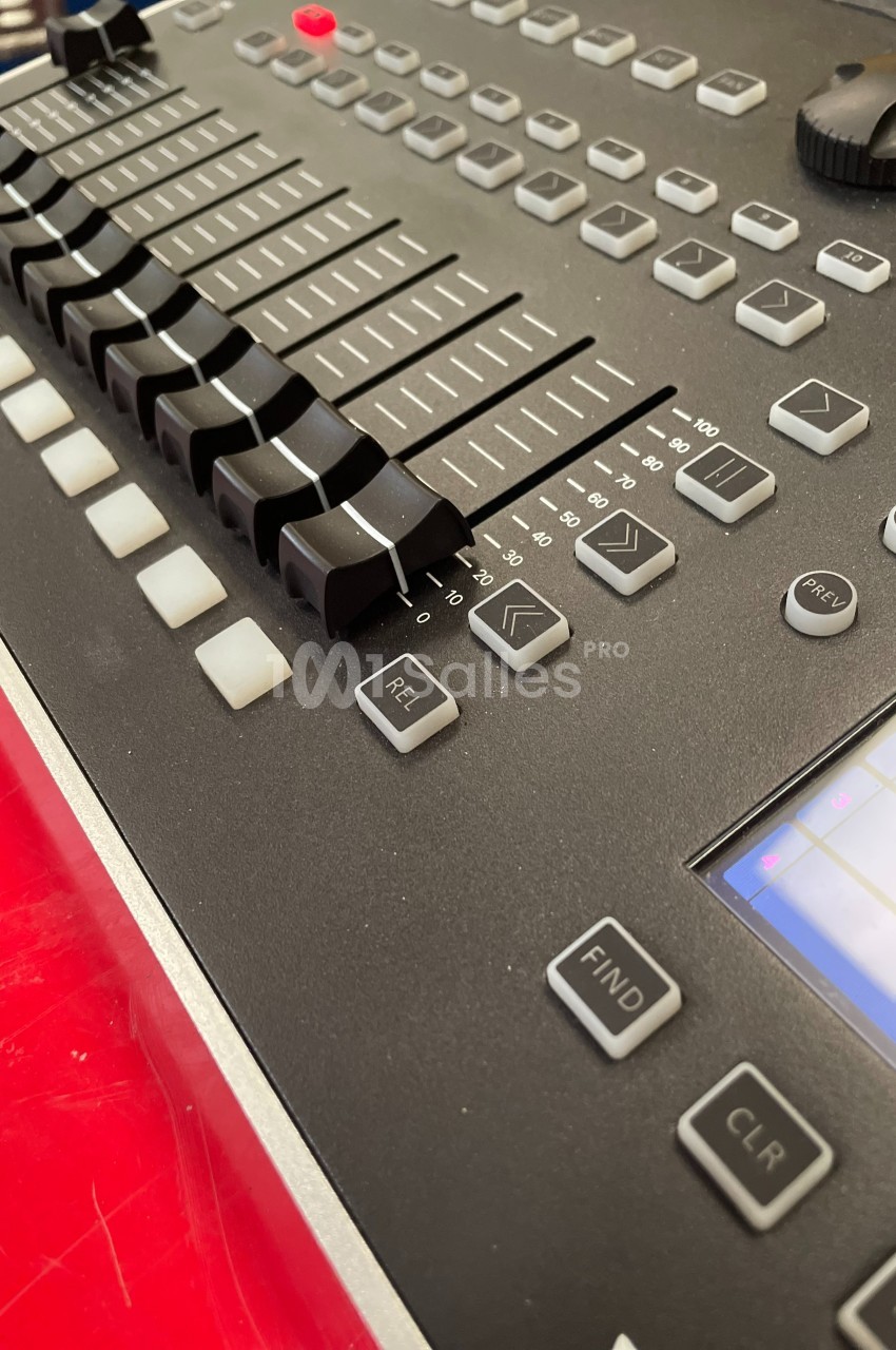 Table de mixage audio avec curseurs, boutons et écran tactile, posée sur une surface rouge.