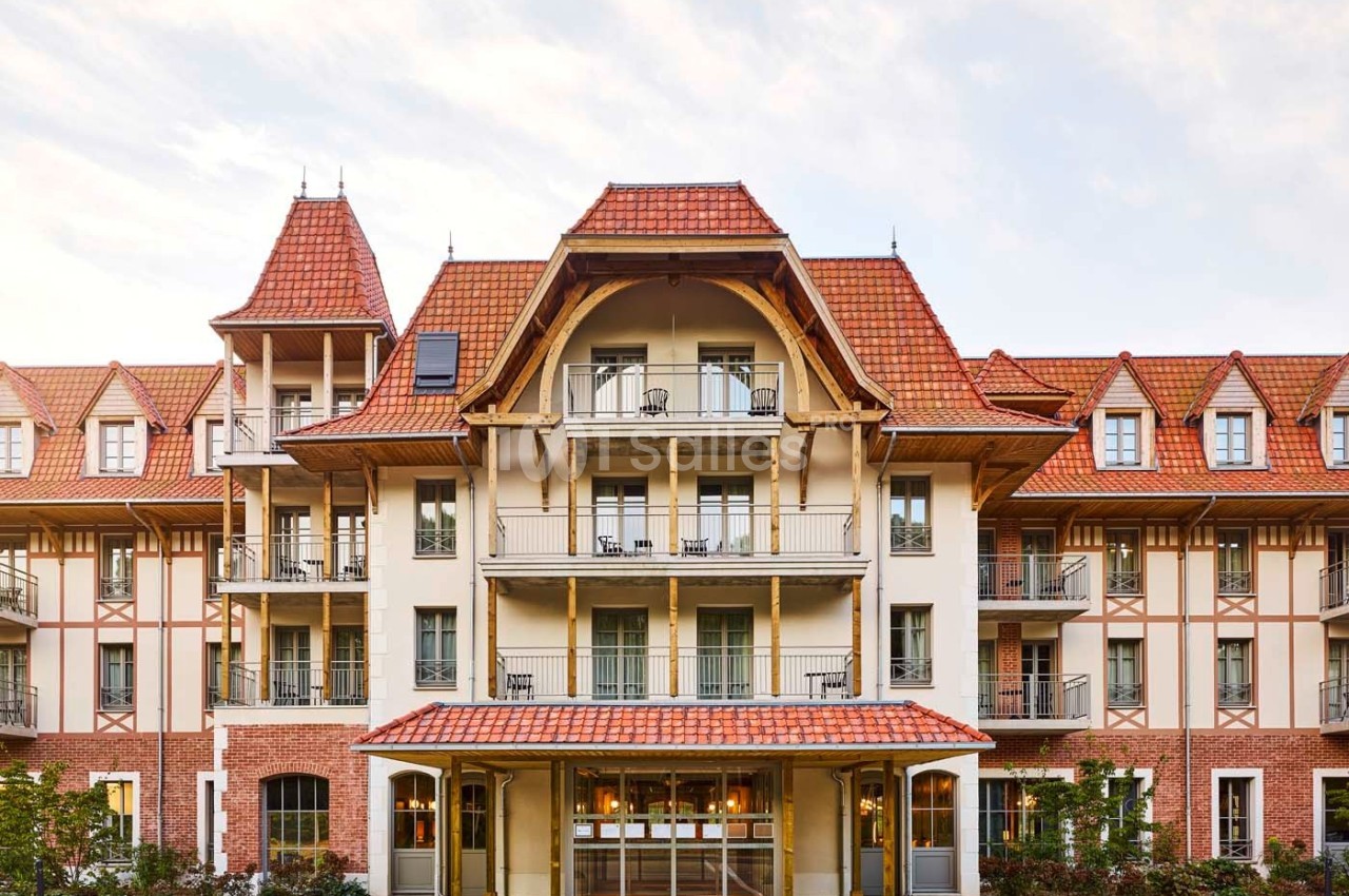 Façade d'un bâtiment à l'architecture traditionnelle avec toit en tuiles rouges et balcons en fer forgé.