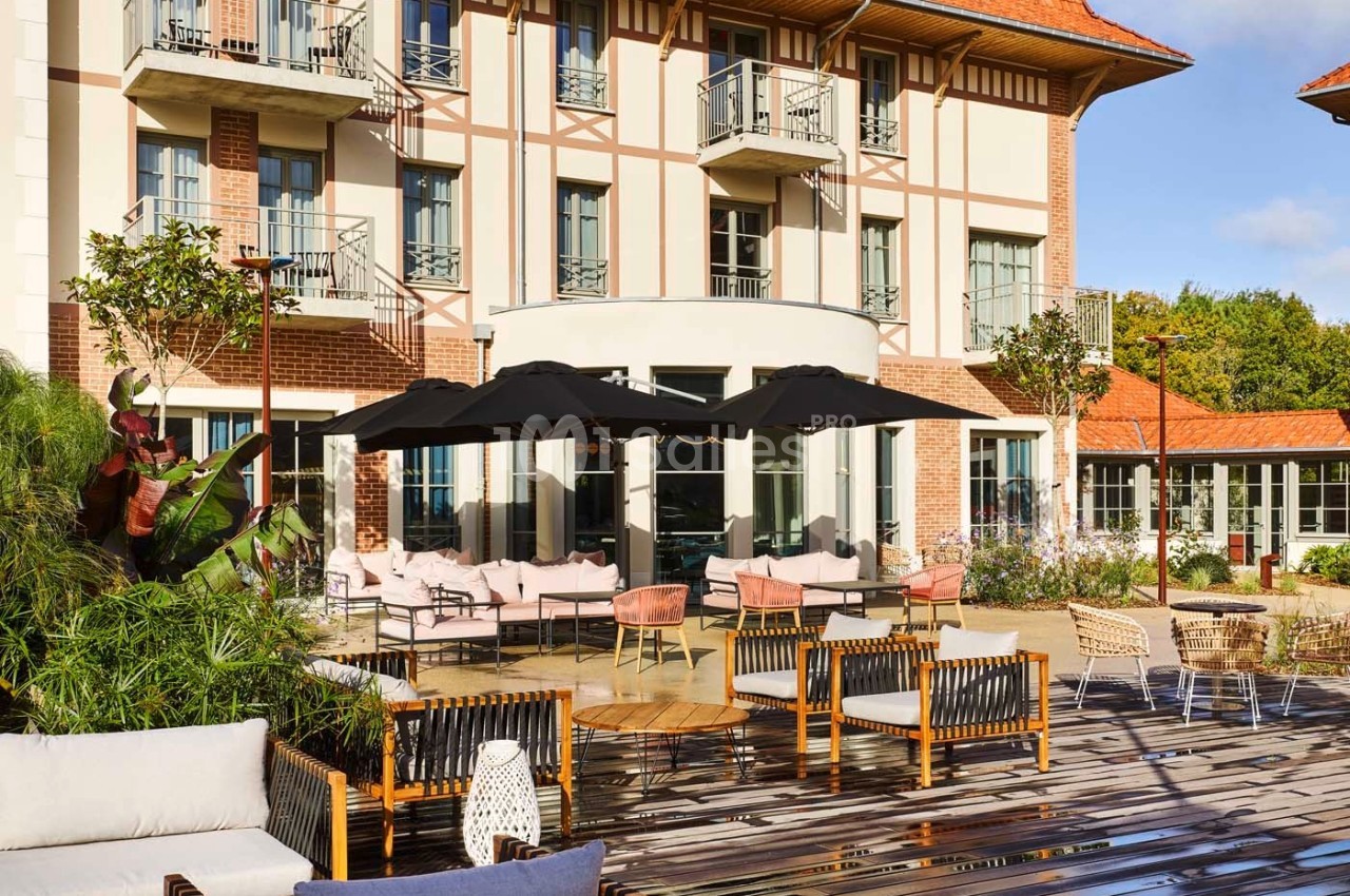 Terrasse en bois aménagée avec des tables, chaises et parasols noirs devant un bâtiment à colombages.