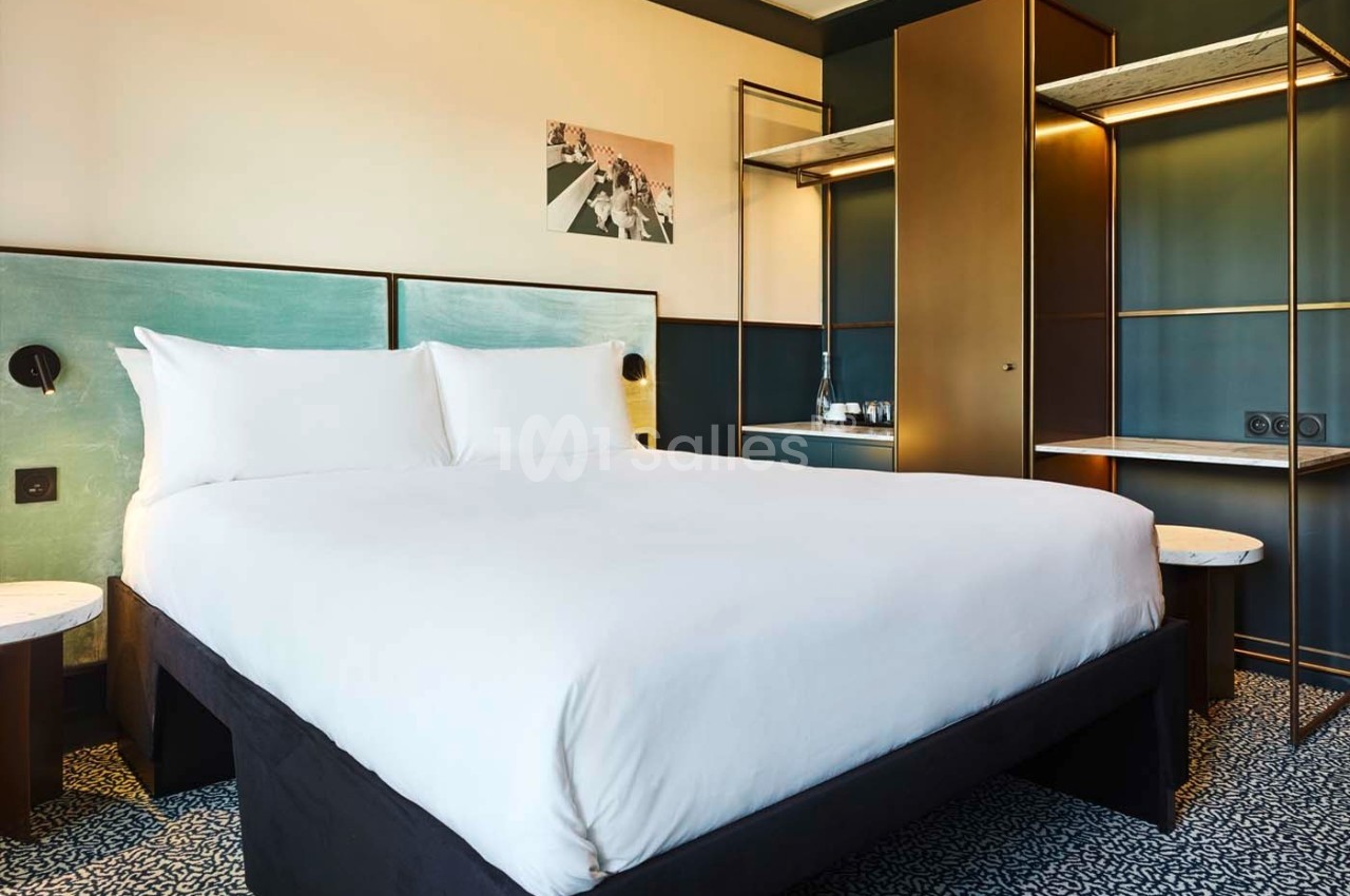 Lit double avec draps blancs dans une chambre moderne, équipée d'une armoire, de tables de chevet et d'un éclairage…