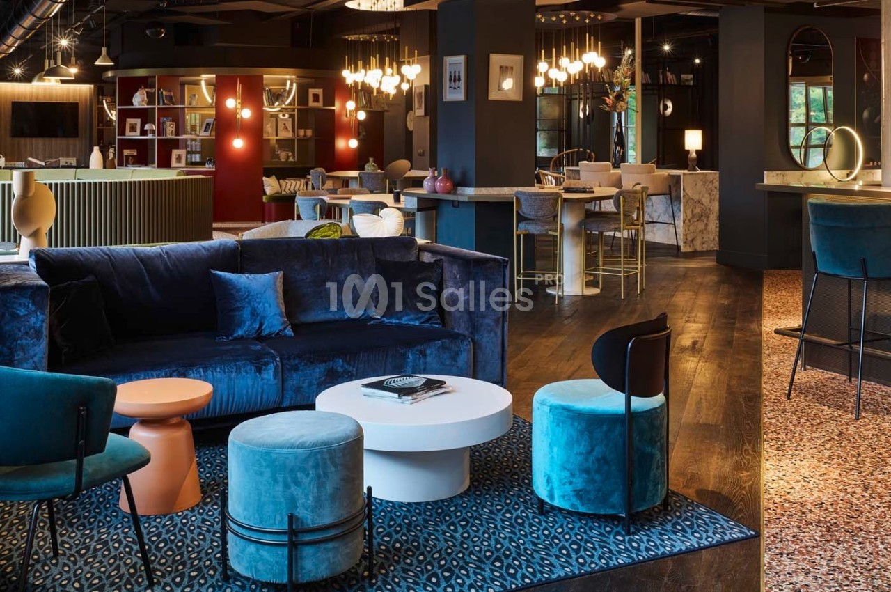 Espace intérieur moderne avec canapé bleu, tables basses, chaises design et éclairage chaleureux.