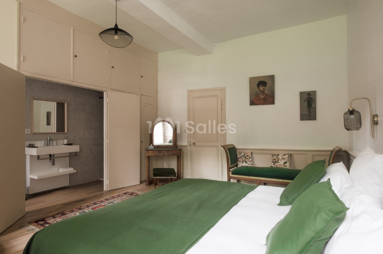 Chambre lumineuse avec lit double, linge de lit vert, mobilier en bois, salle d'eau attenante et décoration murale.