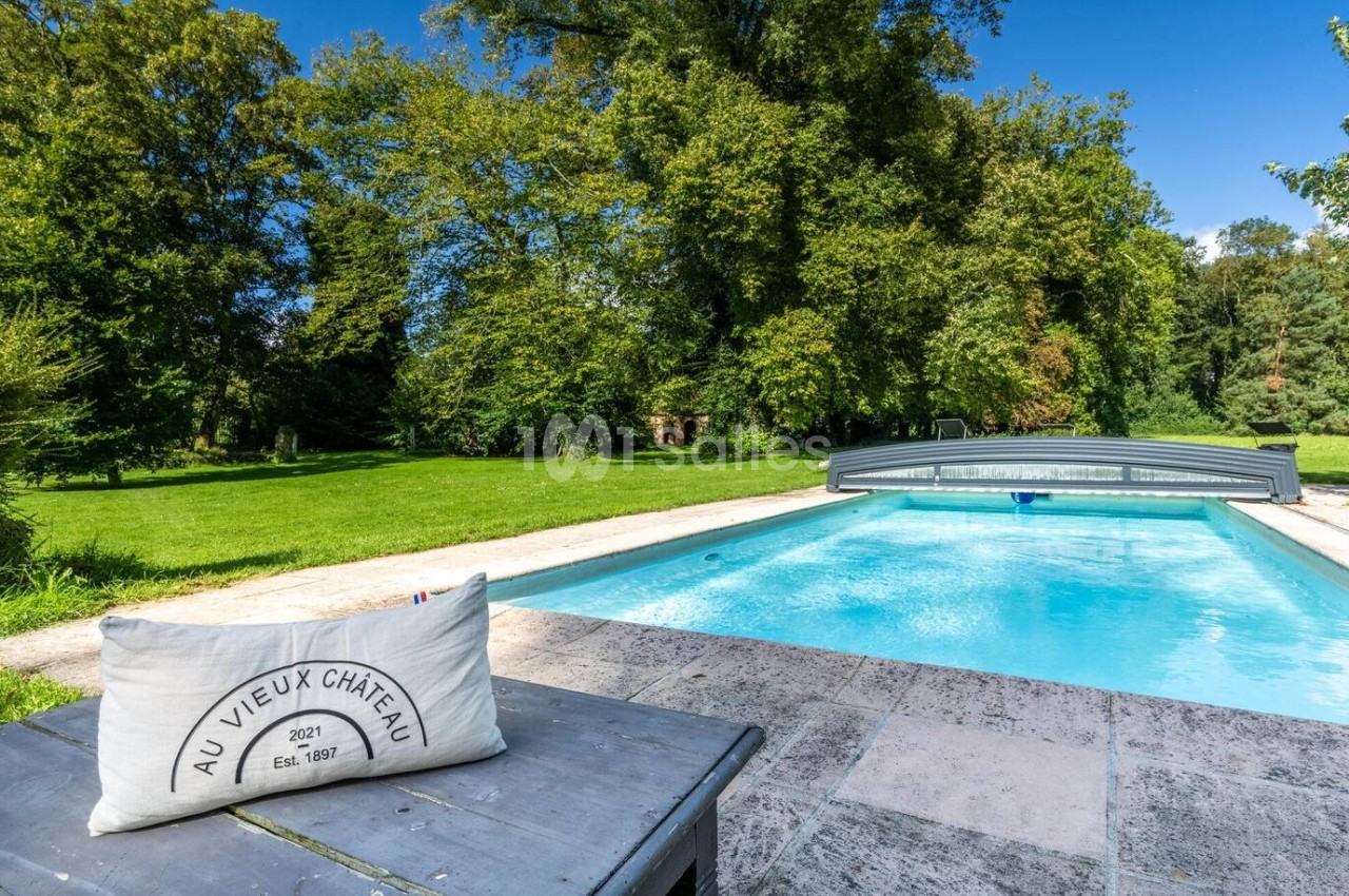 Piscine extérieure avec abri coulissant, entourée de verdure et d'arbres, vue depuis une table en pierre.