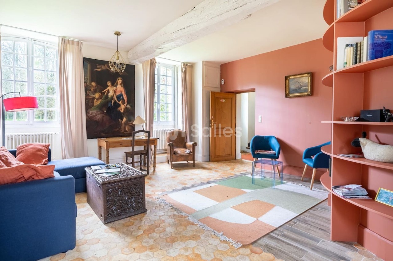 Salon lumineux avec murs terracotta, mobilier éclectique, grande fenêtre, tableau classique et étagère courbée.