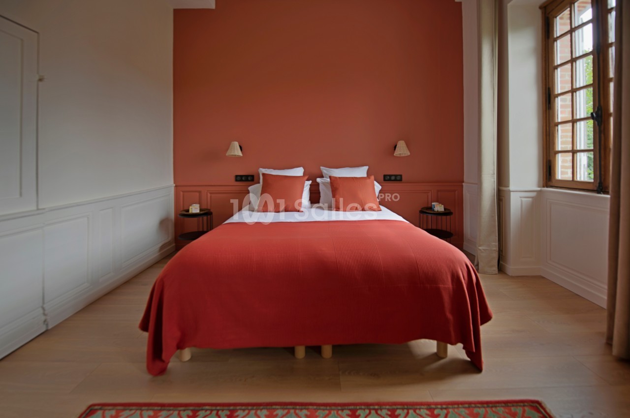 Lit double avec couverture rouge et coussins assortis, encadré par deux tables de chevet, dans une chambre lumineuse.