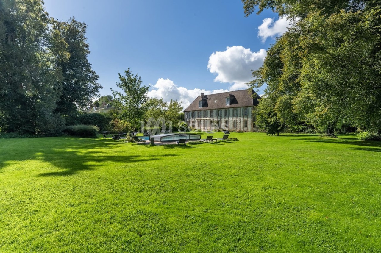 Grande maison en pierre entourée d'un vaste jardin verdoyant avec pelouse, arbres et mobilier d'extérieur.
