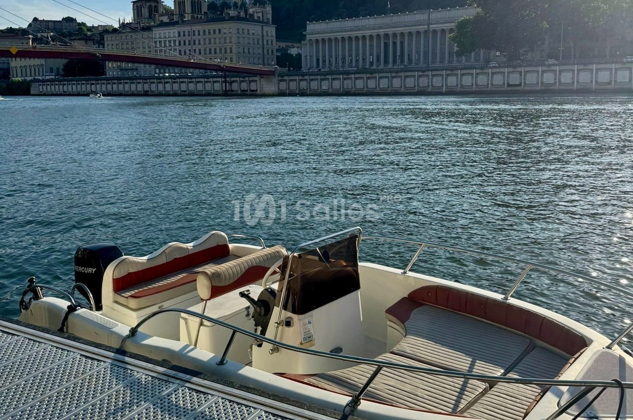 Bateau amarré sur une rivière avec des bâtiments historiques et une colline en arrière-plan.