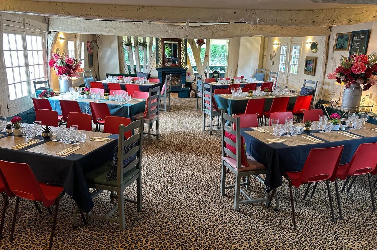 Salle de restaurant décorée avec des tables dressées, chaises colorées et fleurs, dans un cadre rustique avec poutres…