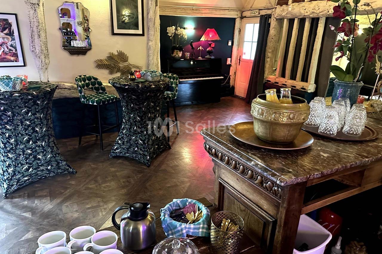 Salle décorée avec un bar en bois, tables hautes, piano en arrière-plan et ambiance chaleureuse.