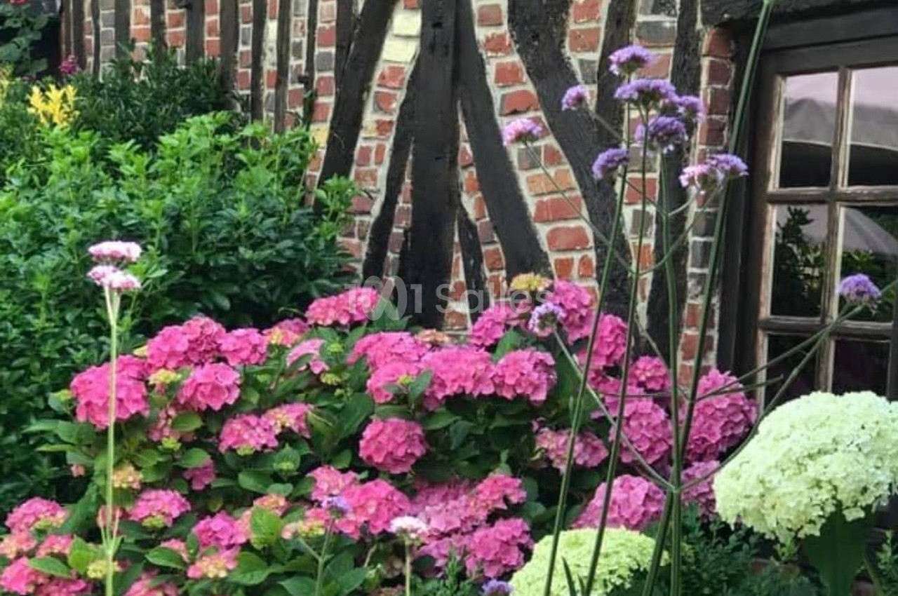 Façade en briques et bois d'une maison, entourée d'hortensias roses et blancs dans un jardin fleuri.