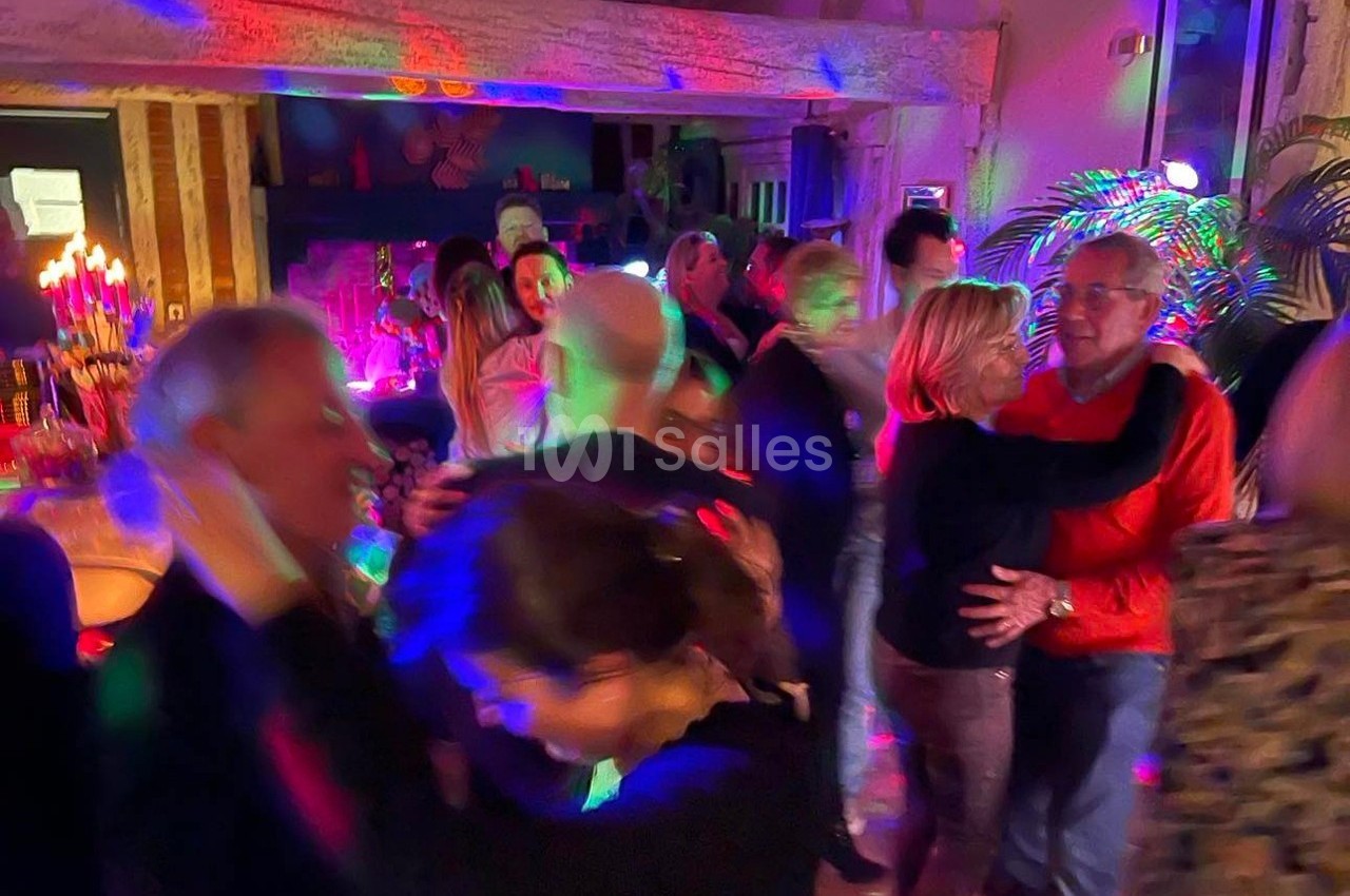 Des personnes dansent dans une ambiance festive avec éclairages colorés dans une salle chaleureuse.