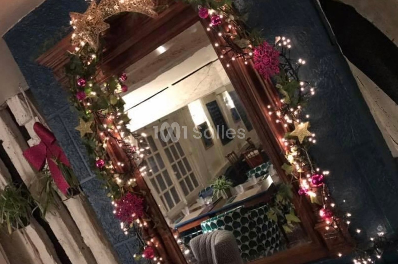 Miroir encadré de guirlandes lumineuses, décoré d'étoiles dorées et de boules roses, reflétant une salle à manger.