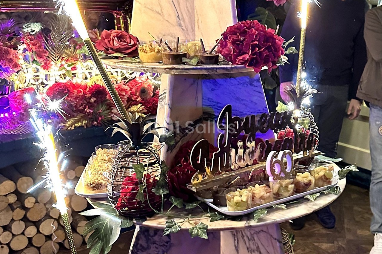 Présentoir décoré avec desserts, fleurs et pancarte ’Joyeux anniversaire 60’ entouré de cierges étincelants.