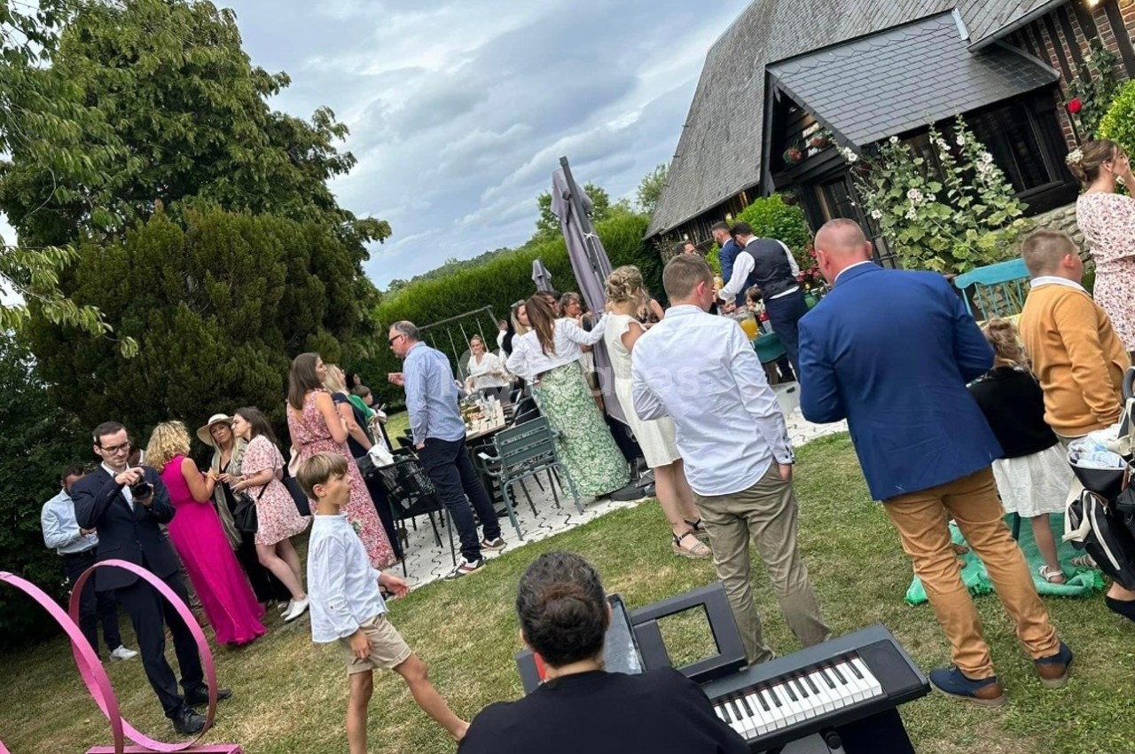 Groupe de personnes rassemblées dans un jardin lors d'une réception en plein air près d'un bâtiment en briques.
