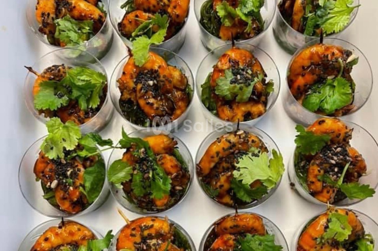 Crevettes marinées servies dans des verrines avec herbes fraîches, graines de sésame et lit de légumes verts.