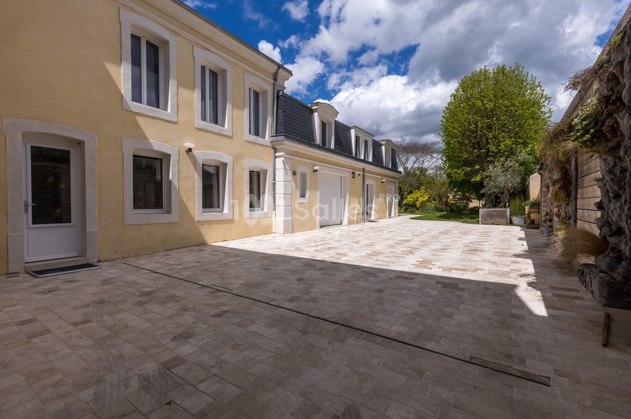 Cour pavée en pierre claire entourée d'un bâtiment jaune à deux étages et d'un mur végétalisé sous un ciel partiellement…