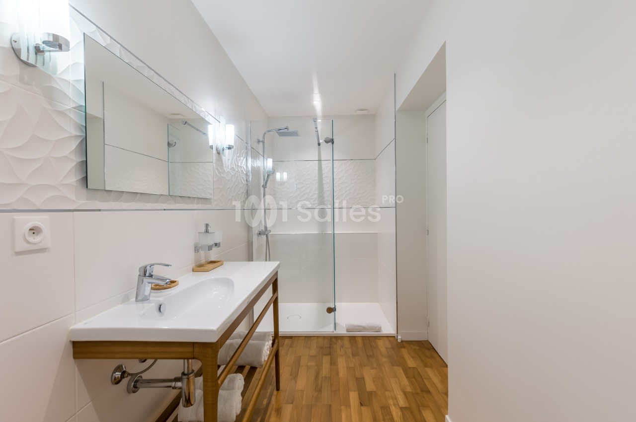 Salle de bain moderne avec douche vitrée, lavabo sur meuble en bois et sol en parquet.