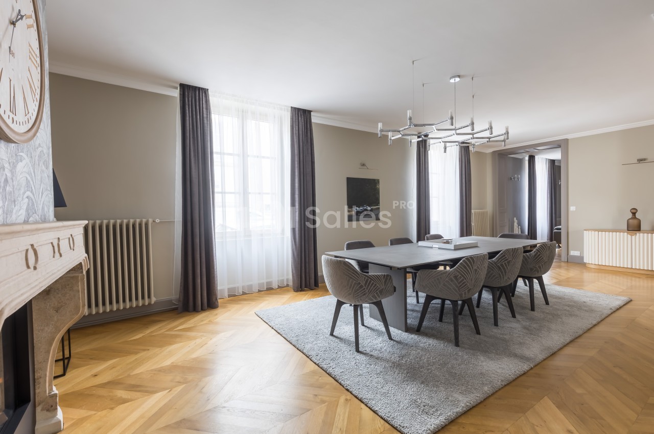 Salle à manger lumineuse avec table grise, chaises modernes, parquet en bois clair et grandes fenêtres avec rideaux.
