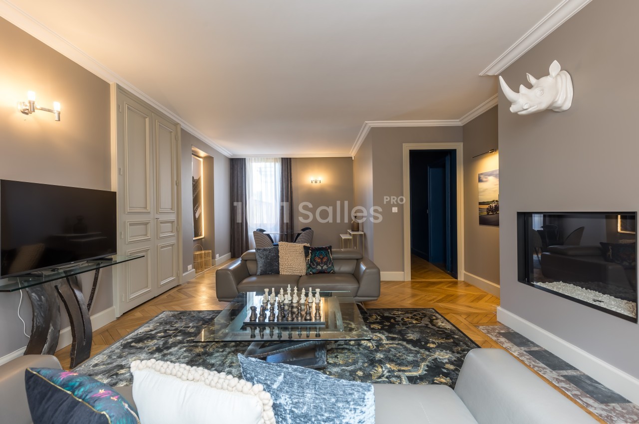Salon moderne avec canapé gris, table basse, échiquier, télévision, cheminée et décoration murale en forme de rhinocéros.