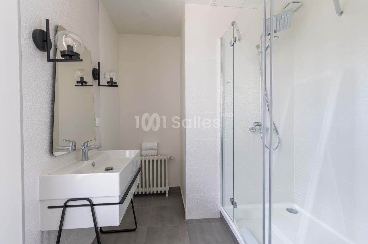 Salle de bain moderne avec lavabo, miroir, douche vitrée et murs blancs.