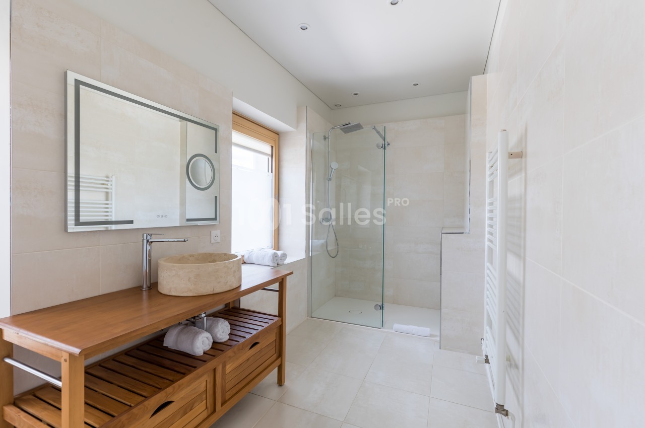 Salle de bain moderne avec douche à l'italienne, meuble en bois avec vasque et grand miroir rectangulaire.