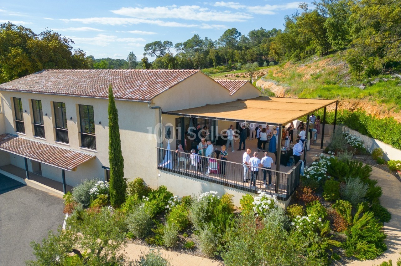 Vue aérienne d'un bâtiment avec une terrasse ombragée où des personnes sont rassemblées, entouré de végétation.