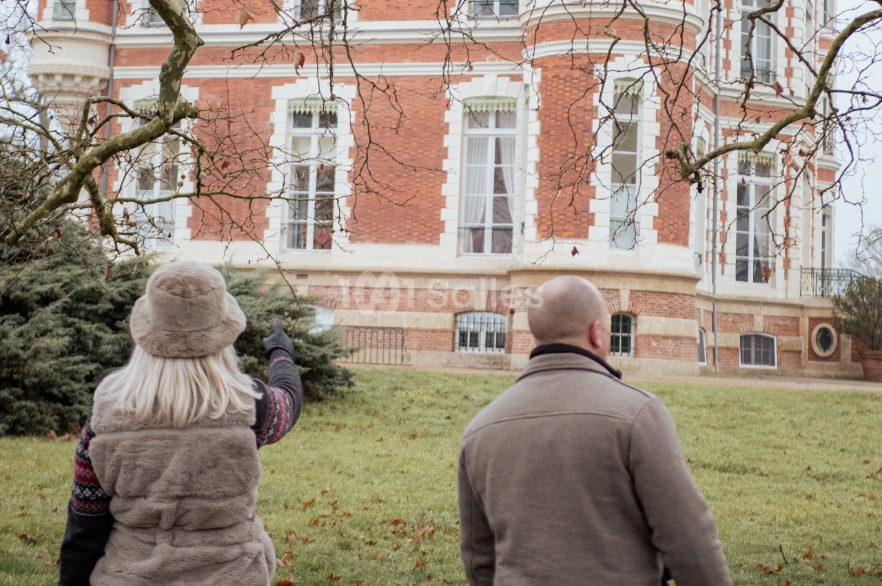 Deux personnes de dos observent la façade d'un bâtiment en briques rouges entouré de verdure.