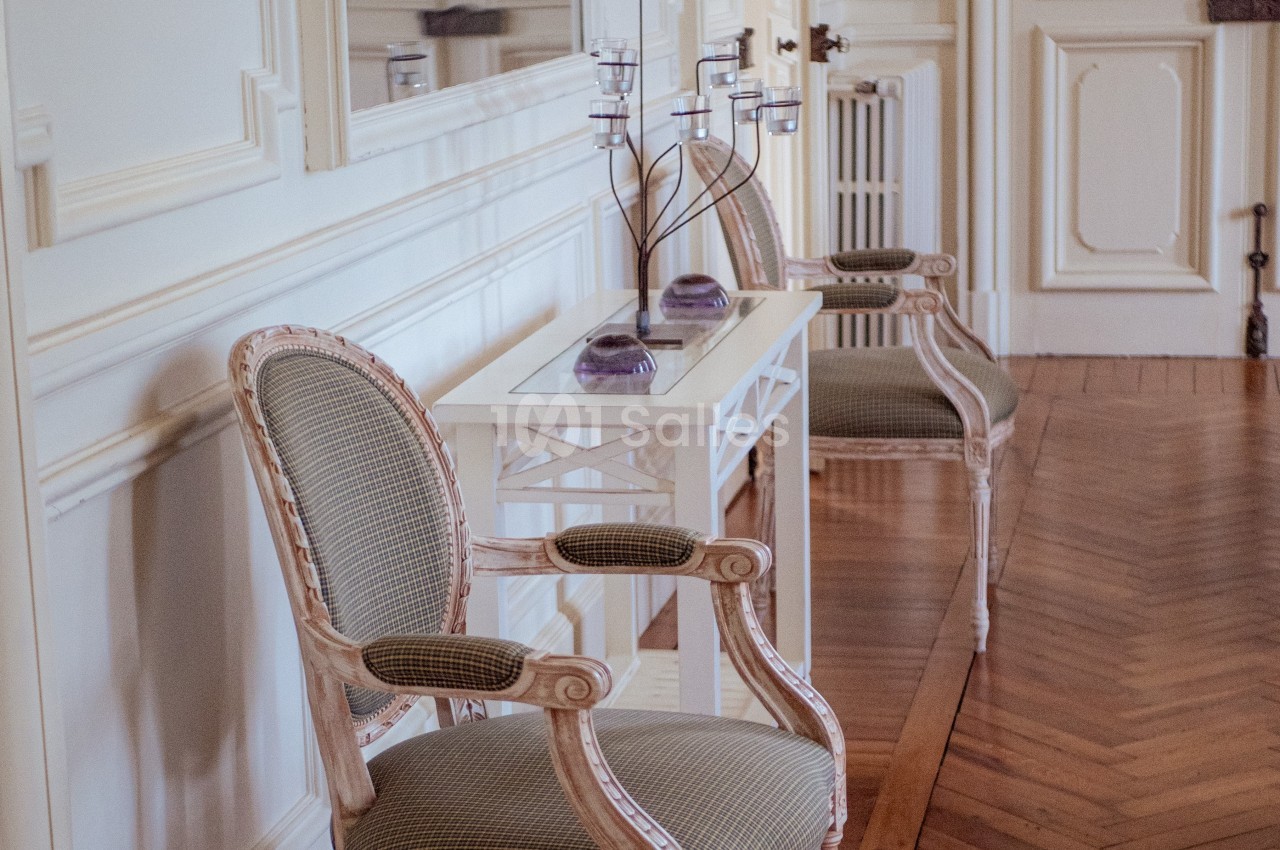 Deux fauteuils anciens encadrent une console blanche ornée de bougeoirs et de décorations violettes dans une pièce élégante.