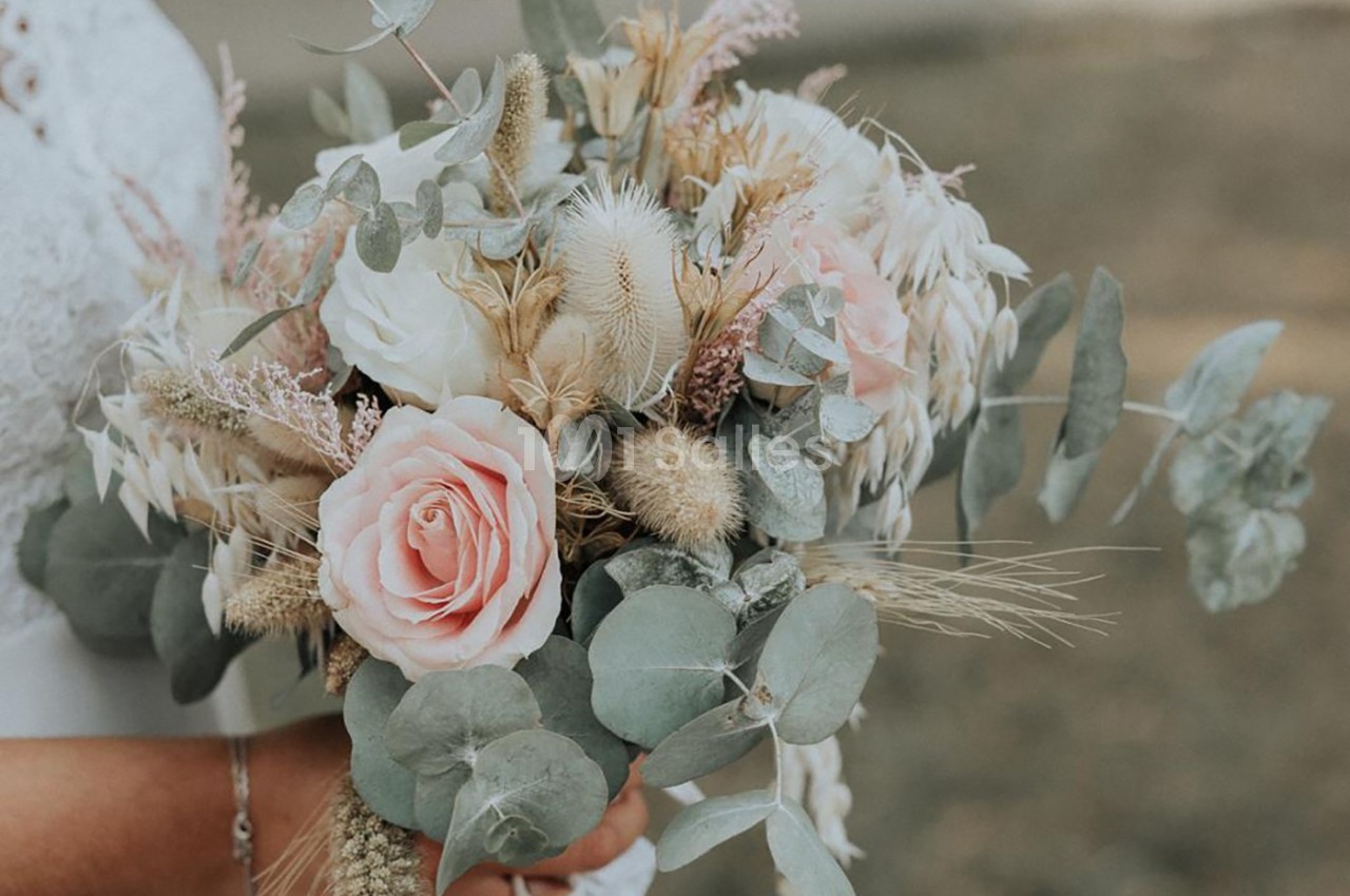 Bouquet de fleurs séchées et fraîches avec roses, eucalyptus et graminées, tenu par une personne en robe blanche.