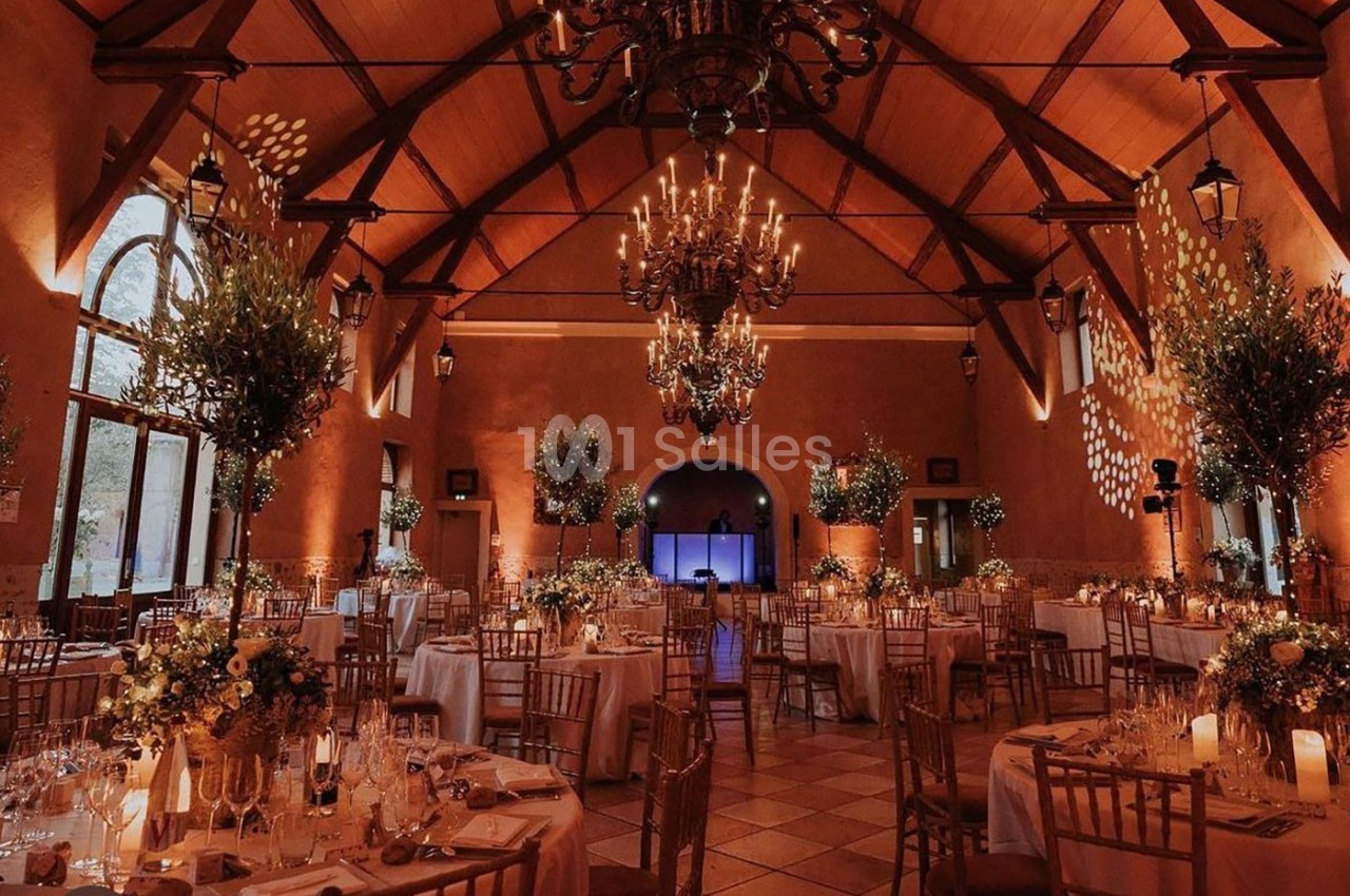 Salle de réception élégamment décorée avec des tables rondes, des chandeliers suspendus et une lumière tamisée.