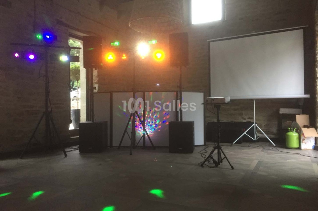 Équipement de sonorisation et éclairage coloré installé dans une salle en pierre avec un projecteur et un écran.