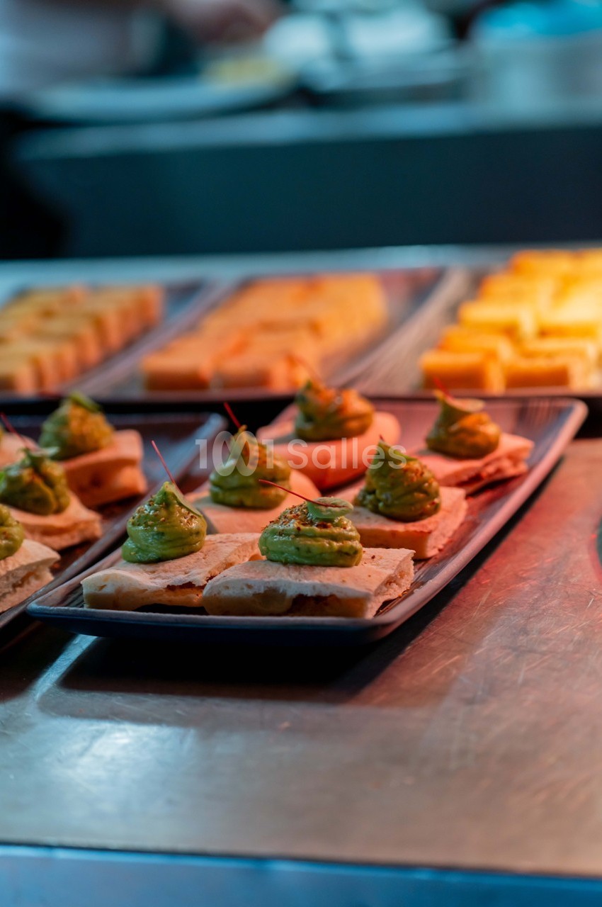 Assiette de toasts garnis de crème verte, disposés sur un comptoir en métal avec d'autres plats en arrière-plan.