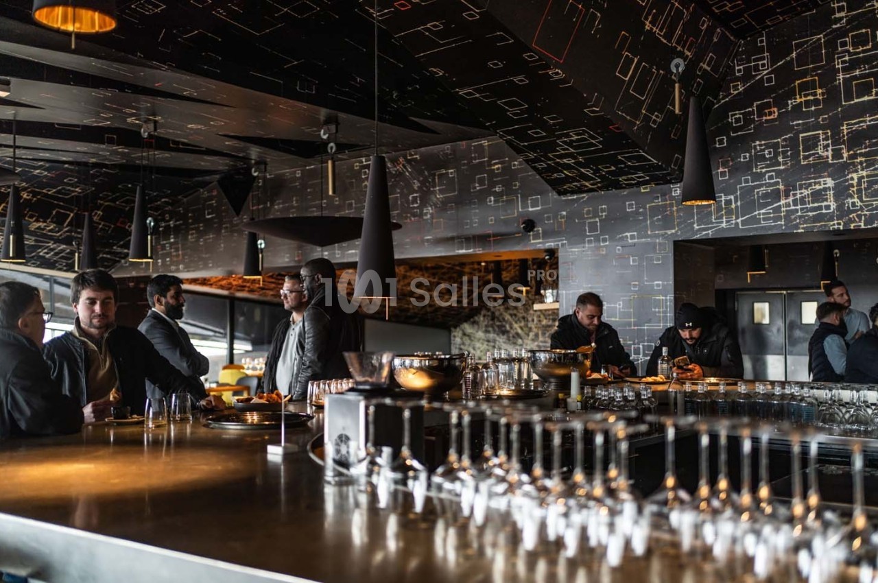 Des personnes discutent autour d'un bar moderne avec un éclairage tamisé et une décoration géométrique sombre.