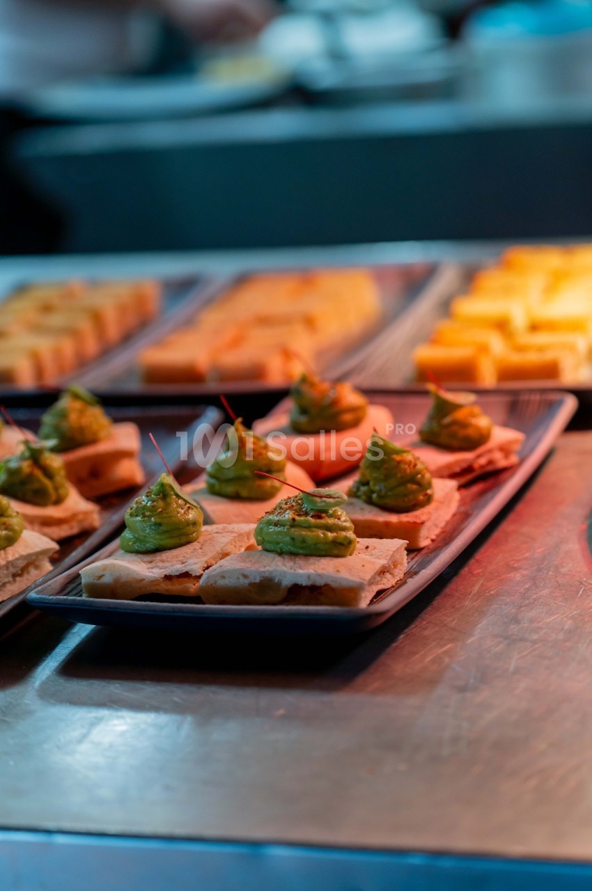 Assiette de toasts garnis de crème verte, disposés sur un comptoir en métal avec d'autres plats en arrière-plan.