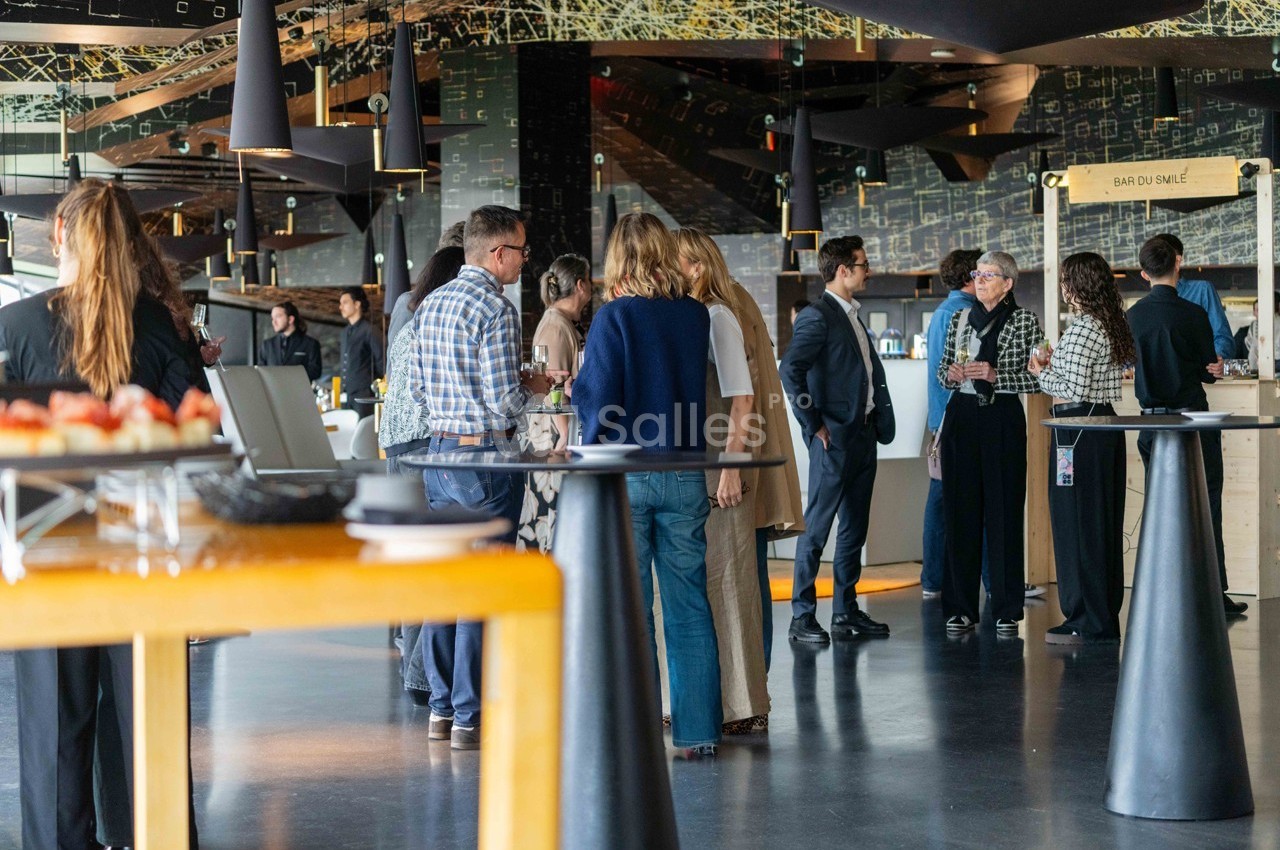 Groupe de personnes discutant debout dans un espace intérieur moderne avec tables et buffet en arrière-plan.