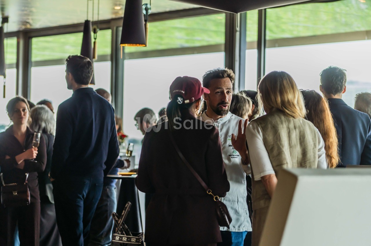 Groupe de personnes discutant dans un espace lumineux avec de grandes fenêtres et des tables en arrière-plan.