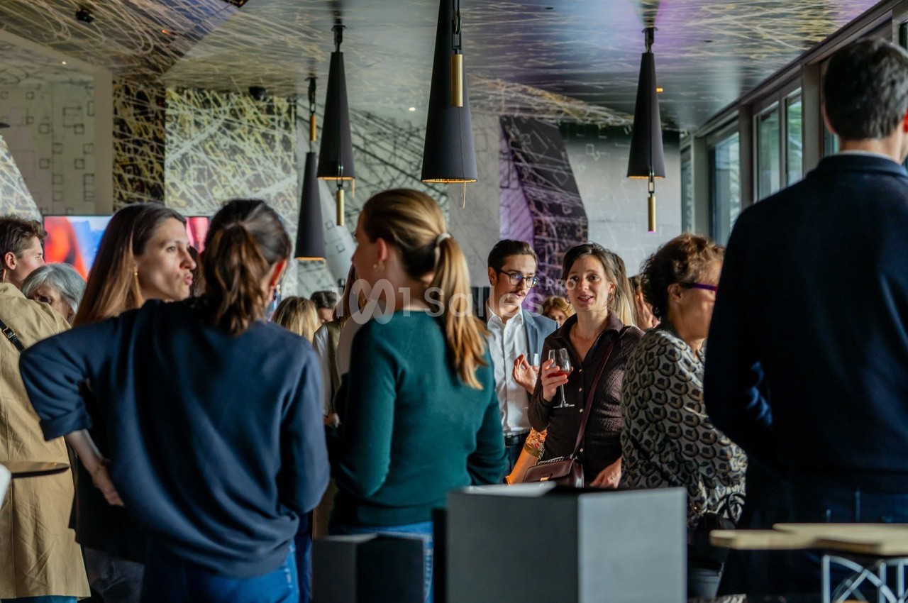 Groupe de personnes discutant dans un espace intérieur moderne avec éclairage suspendu et grandes fenêtres.