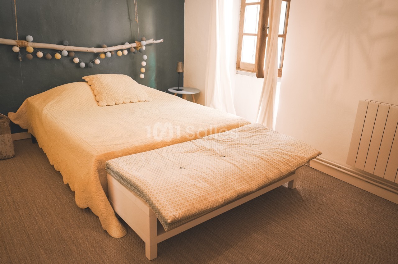 Lit double avec couvre-lit jaune, banc rembourré assorti, mur vert décoré et lumière naturelle d'une fenêtre.