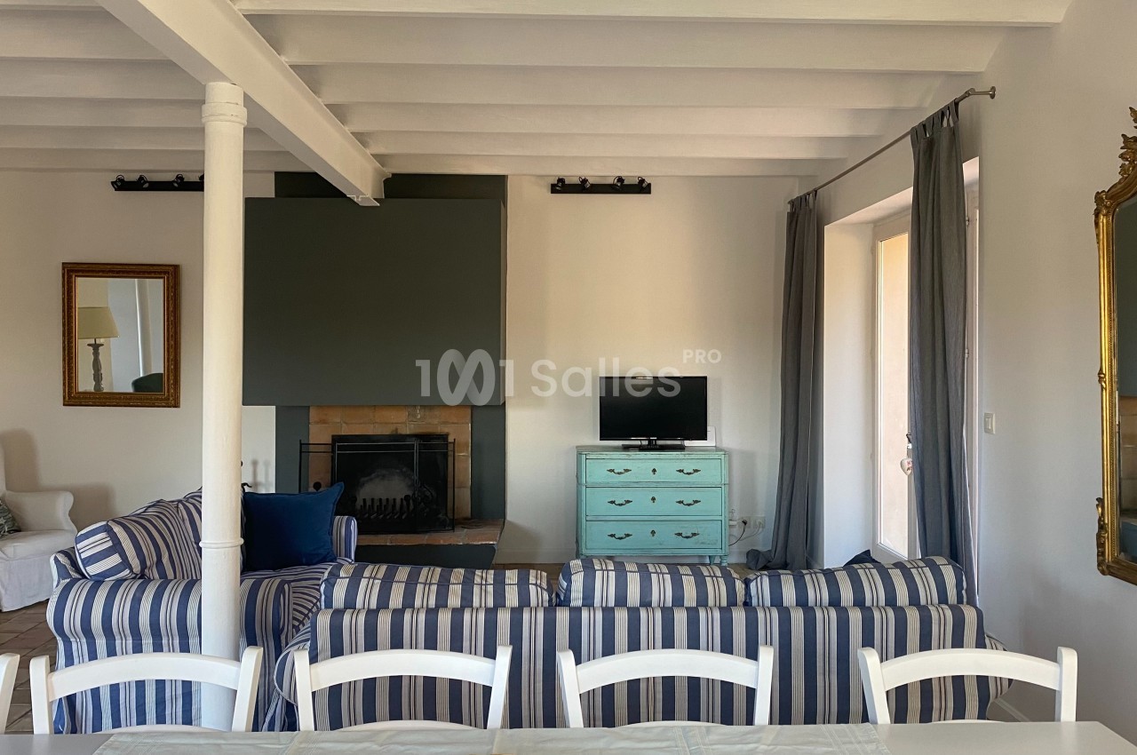 Salon lumineux avec canapé à rayures, cheminée, petite télévision sur une commode turquoise et miroir doré.