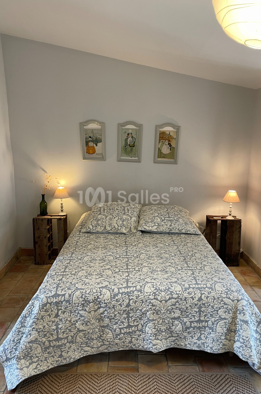 Lit double avec couvre-lit à motifs, encadré par deux tables de chevet en bois avec lampes, dans une chambre lumineuse.