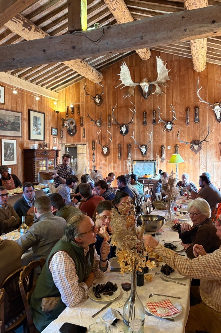 Des convives partagent un repas dans une salle rustique décorée de trophées de chasse et de bois apparents.