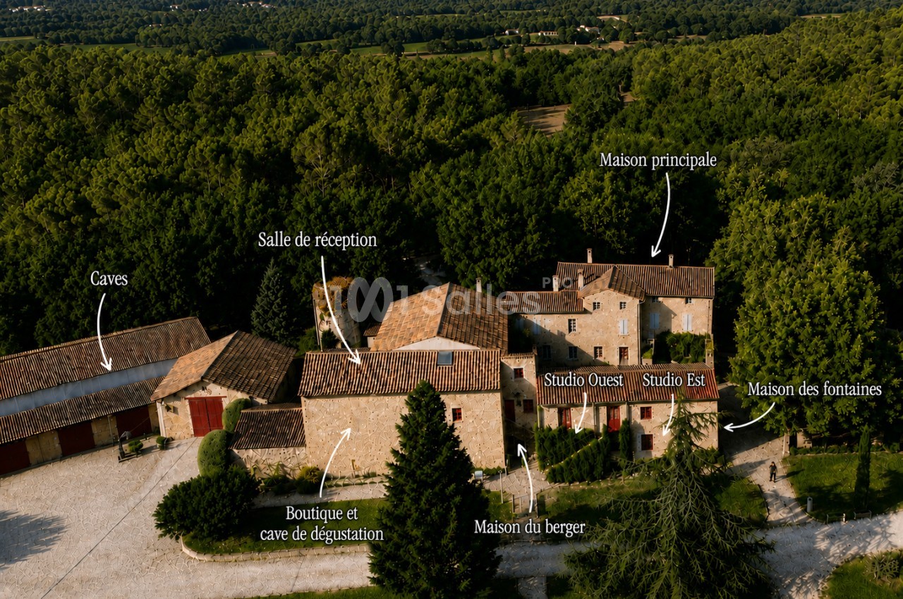 Vue aérienne d'un ensemble de bâtiments en pierre avec toits en tuiles entourés de forêt.