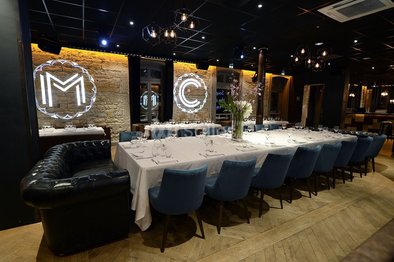 Grande table dressée avec des chaises bleues dans un restaurant élégant, éclairé par des néons et des lumières tamisées.