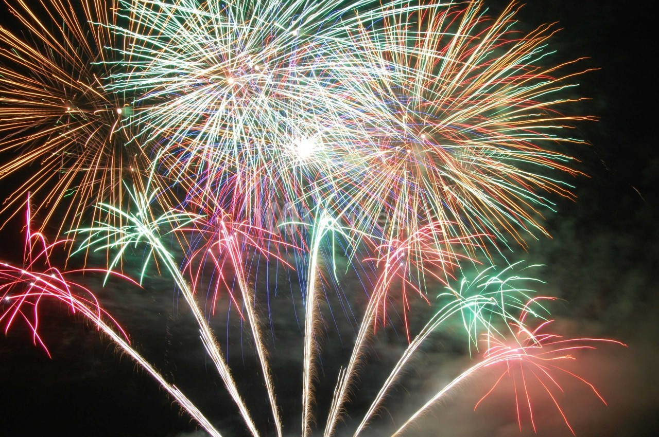 Feux d'artifice multicolores éclatant dans le ciel nocturne avec des traînées lumineuses.