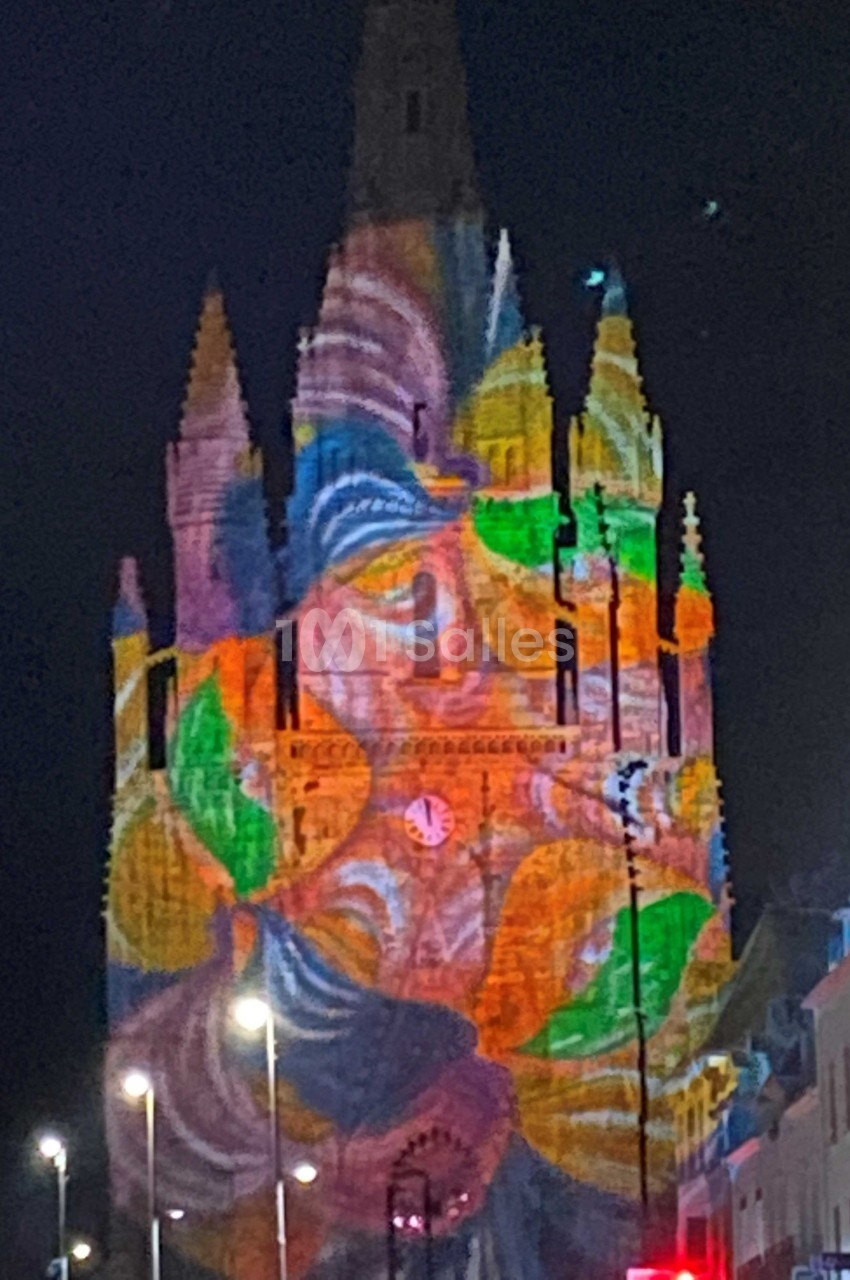 Projection lumineuse colorée représentant un visage sur la façade d'une église gothique de nuit.