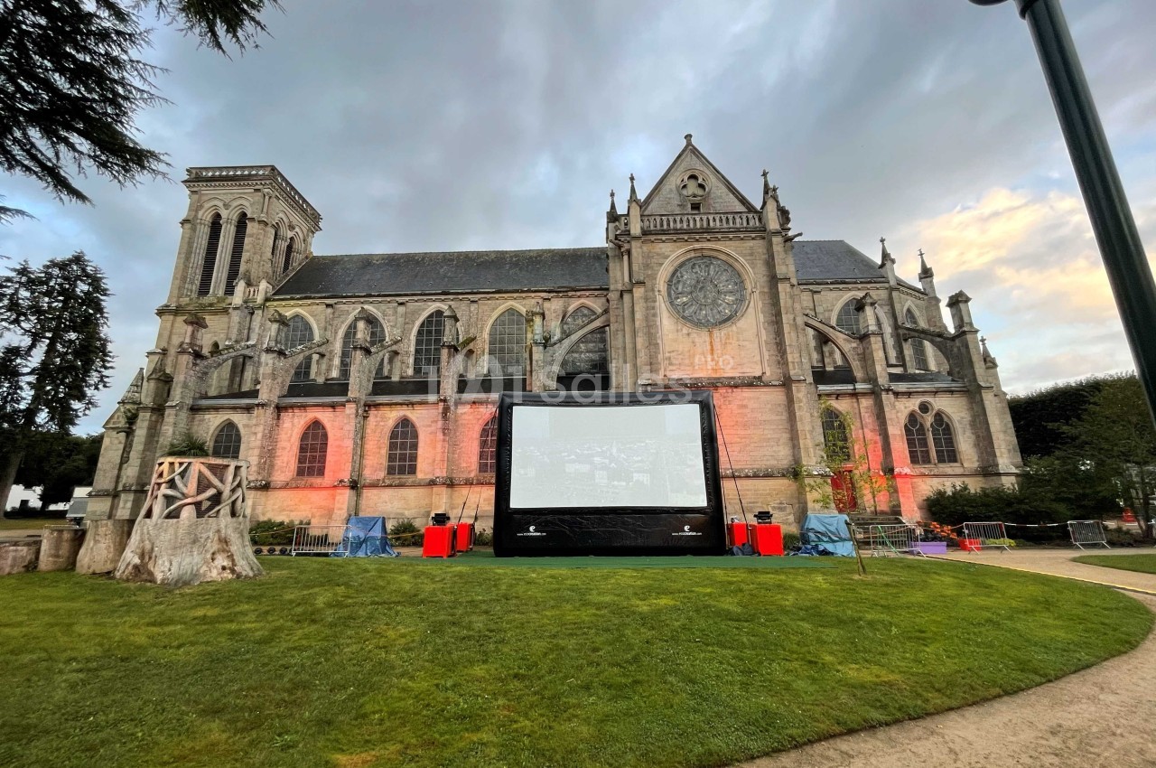 Écran de projection installé sur une pelouse devant une église gothique éclairée à la tombée du jour.