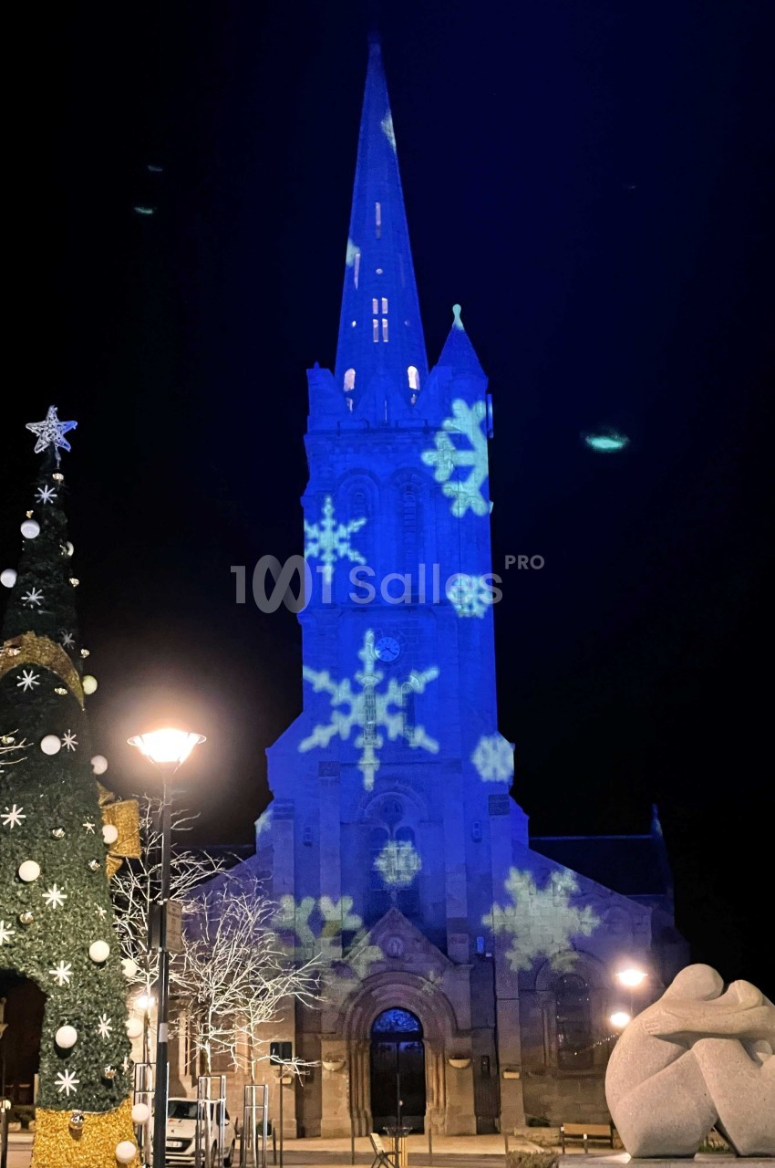 Église illuminée en bleu avec des motifs de flocons de neige, décorations de Noël et sculptures au premier plan.
