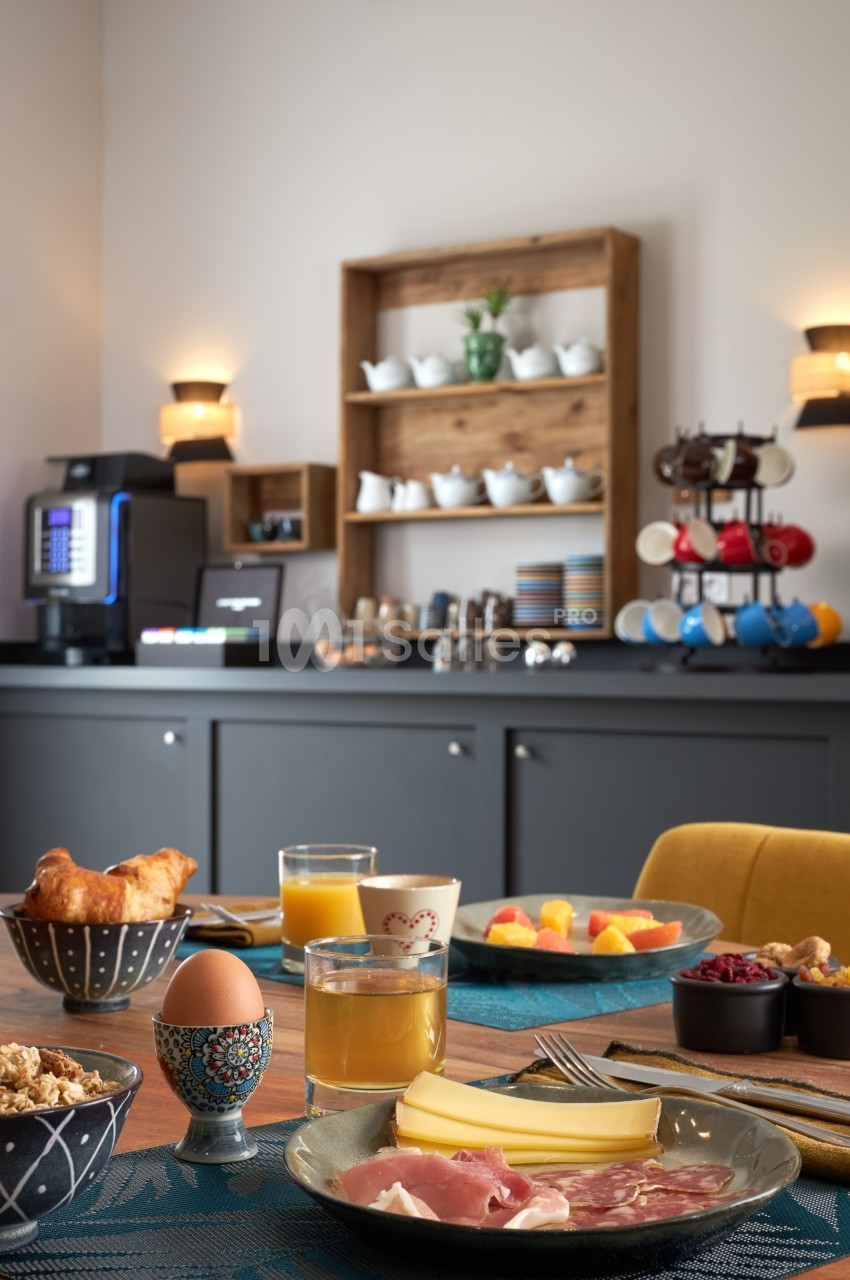 Petit-déjeuner servi avec charcuterie, fromage, fruits, viennoiseries, œuf à la coque et boissons, dans une salle lumineuse.