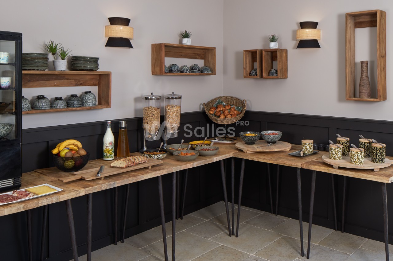 Buffet de petit-déjeuner avec céréales, fruits, viennoiseries et boissons, disposé sur des tables en bois dans une salle…