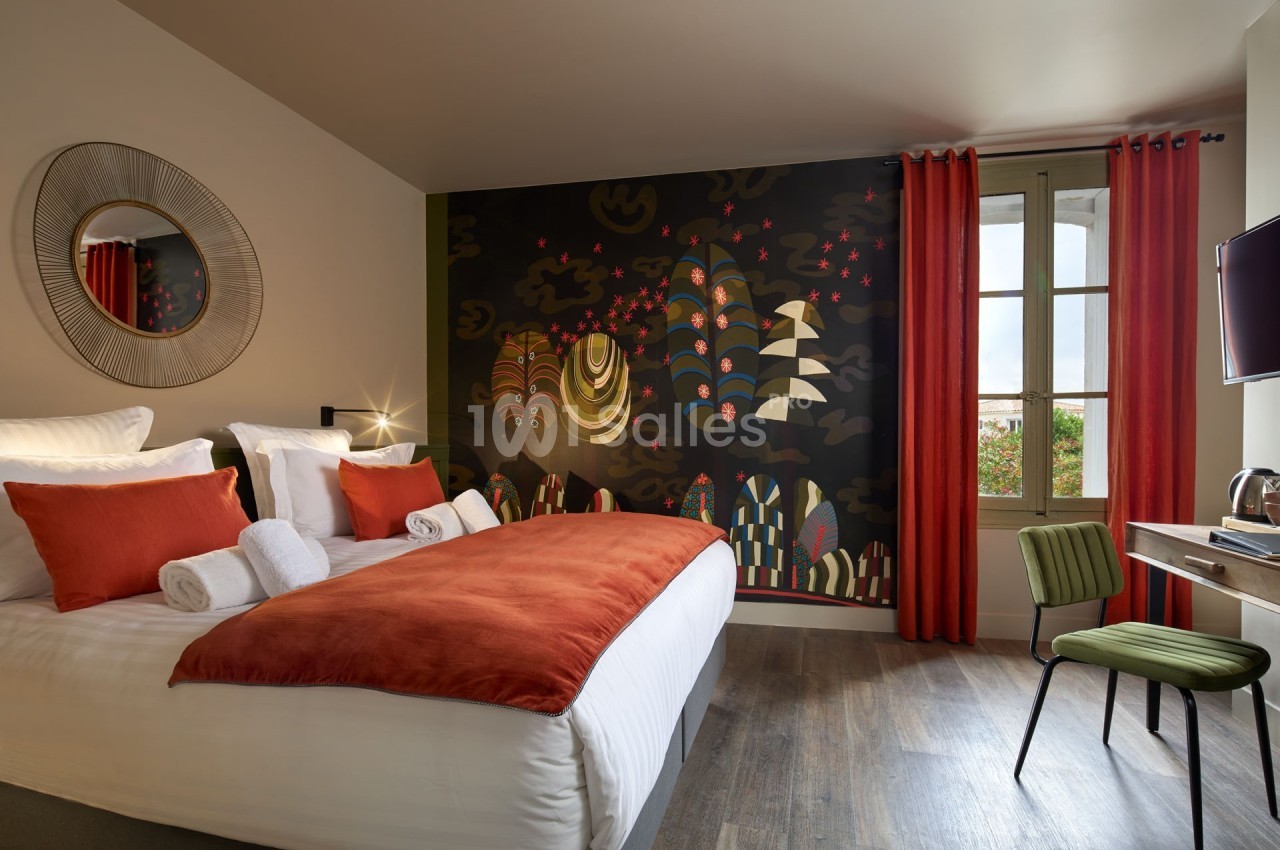Chambre moderne avec lit double, tête de lit décorée d'une fresque colorée, fenêtre et bureau avec chaise verte.